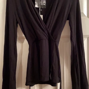 Omlott topp med utsvängda armar  - En snygg omlottblus i svart med utsvänga armar, helt OANVÄND med prislapp på. Den har även ett band vid midjan som man kan forma och knyta hur man vill. Ursnygg och super skön. I storlek xs, passar även xs,s,m då den är stretchig och anpassar sig till din kroppsform💓