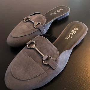 Slip-in skor stl 40 - Säljer mina gråa slip-ins. De är helt oanvända (bara testade) och supersköna! De är vida i fram och har ett litet spänne. Minns tyvärr inte märke!