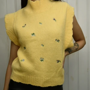 Stickad slipover - En stickad slipover i mjuk kvalite. Slipovern har volang detalj kring halsringning, ärmhål och nedtill. Broderad med små blommor. Aldrig använd. 