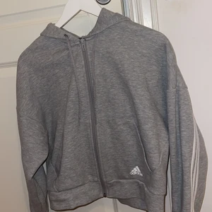 Adidas kofta - Säljer denna zip kofta från adidas. Ränder som går från arm till arm som ni ser på bilden på ryggen. Ljusgrå färg och lite mer ”croppad” i modellen än vanligare koftor storlek S men passar M. Använd två gånger