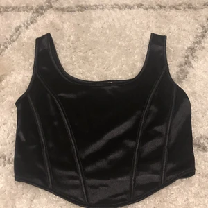 Svart korsett - Säljer ett svart ”korsett” liknande linne i ett silkesmaterial från bikbok. Den är i stl M och i ett väldigt bra skick då den lampor är använd