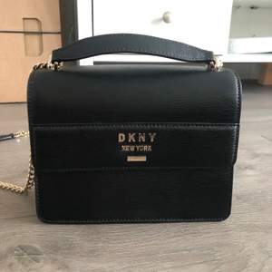 Supersnygg mindre väska från DKNY. I nyskick och aldrig använd! Svart och guldiga detaljer. Väskan skickas som spårbart paket med posten.