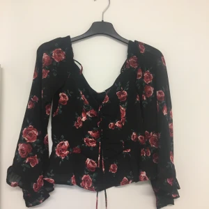 Mönstrad blus - INTRESSEKOLL. Svart blus med rödrosa rosor på. Knytning fram. Sparsamt använd, säljes pga kommer ej till användning. Buda. Startpris är 100kr.