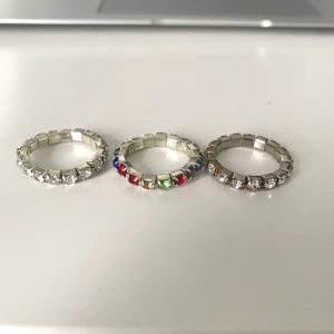 Tre coola strass-ringar  - Tre ringar med stenar. En med färgade stenar och två med silverstenar. Den ena  är helt silverfärgad och den andra har lite guld mellan stenarna (se bild 2). Ringarna är 17mm men töjbara så passar även större. Inte åkte silver. Köparen står för frakt. 