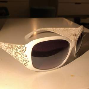 Ett par vita solglasögon med coolt mönster på bågarna, inget märke och i plast. Själva ”glas” delen har rätt så många repor och de är rätt så lätta! Lagade men fixade!