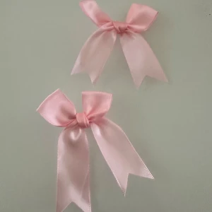 Rosa rosett hårspännen - Två söta hårspännen med ljusrosa rosetter i satinband. Perfekta som accessoar för att piffa upp frisyren. Rosetterna har metallspänne på baksidan för enkel fastsättning i håret.