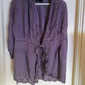 Lila omlott blus från Vero Moda - Säljer en lila omlott blus från Vero Moda i storlek XS. Jackan har knytning i midjan och långa ärmar. Materialet är en blandning av bomull och viskos vilket gör den mjuk och lätt. Tyvärr så har jag inte lyckats strula den något bra. Den blir lätt skrynklig