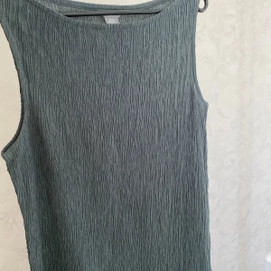 Grå/grön  ärmlös långklänning  - Säljer en stilren grå/grön långklänning från H&M med strukturerat tyg. Klänningen är ärmlös och har en rak, enkel passform som passar perfekt till sommaren. Tillverkad i ett mjukt och bekvämt material.
