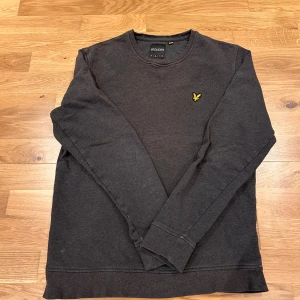 Mörkgrå sweatshirt från Lyle & Scott - Säljer en stilren mörkgrå sweatshirt från Lyle & Scott med rund halsringning och klassisk gul logga på bröstet. Tröjan har långa ärmar och ribbade muddar vid ärmslut och nederkant. Perfekt för en avslappnad look. Nyskick.                    Nypris 850 kr, pris kan diskuteras 