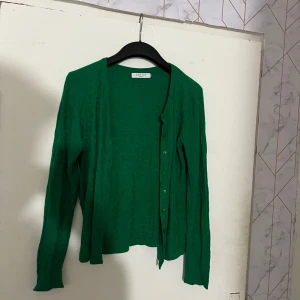 Grön kofta från Costes Basic - Snygg grön kofta från Costes Basic med långa ärmar och knappar framtill. Perfekt att slänga över en topp för en enkel men stilren look. Koftan är i ett mjukt material och har en klassisk passform.