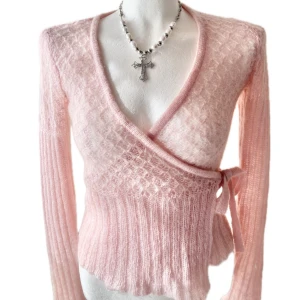 Ljusrosa omlottkofta i mohairmix - Superfin ljusrosa omlottkofta med knyt i sidan. Tröjan är stickad i ett fluffigt mohairliknande material med diskret mönster och ribbade partier. Djup v-ringning och långa ärmar 🌸