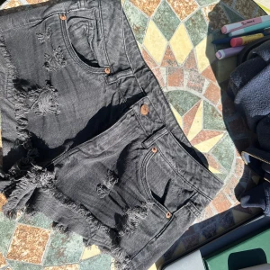 Svarta lågmidjade jeansshorts med fransar - Säljer ett par svarta jeansshorts från Divided med råa fransade kanter och slitna detaljer framtill. Klassisk femficksmodell med knapp och dragkedja. Perfekta för sommardagar och festivaler. Lågmidjade o tyvärr för små för mig:(