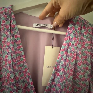 Blommig långärmad klänning från Adoore - Säljer en superfin blommig klänning från Adoore i storlek 34. Klänningen har v-ringning, långa ärmar och ett rosa, blått och grönt blommönster på ljuslila botten. Perfekt för vår och sommar!