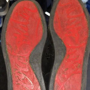 Svarta sneakers från Christian Louboutin - Säljer ett par svarta sneakers från Christian Louboutin med klassisk röd sula och snörning. Skorna är i mocka och har rund tå samt platt sula. Perfekta för dig som vill ha en stilren och lyxig look.