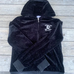 Svart velour hoodie från Juicy Couture - Säljer en svart glittrig hoodie från Juicy Couture i mjuk velour. Jackan har dragkedja, huva och logga både fram och bak. Perfekt för dig som gillar en lyxig och bekväm stil.