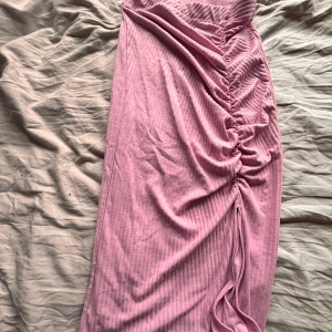 Rosa/lila ribbad kjol med slits - Säljer en rosa/lila ribbad kjol med snygg snörning längs sidan som ger en cool rynkad effekt. Klänningen är figurnära och har en mjuk känsla, perfekt för dig som gillar trendiga detaljer och vill sticka ut.