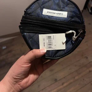 Blå quiltad rund handväska från Carin Wester  - Säljer en rund, quiltad handväska från Carin Wester  i blått med svarta detaljer. Väskan har dragkedja runtom och ett diskret mönster. Perfekt för dig som vill ha en unik accessoar med plats för det viktigaste.