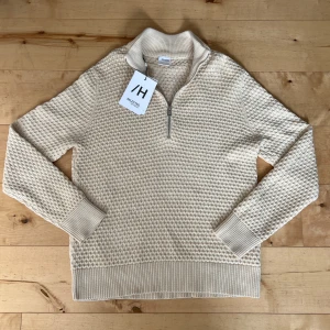 Beige stickad halvzip - Säljer en beige stickad tröja från Selected med halv dragkedja och hög krage. Tröjan har ett strukturerat mönster och ribbade muddar vid ärmslut och nederkant. Perfekt för lager-på-lager under kyliga dagar. Tröjan är aldrig använd och lappen finns kvar. Nypris 699kr