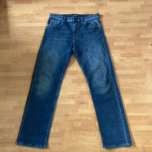 Blå jeansbyxor från Replay - Klassiska blå jeansbyxor från Replay med raka ben och femficksdesign. Byxorna har normal passform och tydliga sömmar, samt Replay-logga på bakfickan och läderpatch i midjan. Perfekta för en avslappnad stil. Modell Thad.                                                                   Priset är inte hugget i sten, skriv om ni har någon fråga