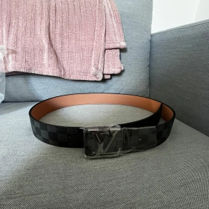 Svart rutigt bälte från välkänt märke  - Säljer ett svart bälte. Bältet är gjort i skinn och har en brun insida. Perfekt accessoar för att lyfta din outfit.