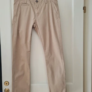 Beige chinos från Cubus - Snygga beige chinos från Cubus med slim passform och stretch för extra komfort. De har en klassisk design med knappar och dragkedja framtill samt fickor både fram och bak. 100% bomull. Waist 30. Kan hämtas i Vallentuna.