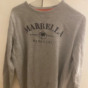 Grå sweatshirt med tryck från Berkeley - Grå sweatshirt med texten 'Marbella Berkeley' och palmtryck framtill. Rund halsringning och långa ärmar. Perfekt för en avslappnad stil.