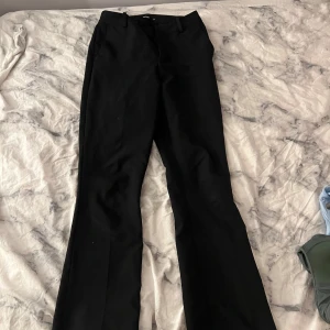 Svarta bootcut kostymbyxor Bikbok - Svarta kostymbyxor från Bikbok i storlek 36. Snygg bootcut-modell med klassisk midja och diskret dragkedja. Materialet är mjukt och har en lätt glansig finish som ger en dressad vibe. Perfekta till en cool outfit med sneakers eller klackar. Ena fickan på insidan blev ett hål sydde ihop (se sista bild)