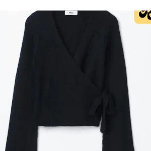 Svart omlottopp med knyt - Svart omlottopp från Gina Tricot med långa ärmar och knyt i sidan. Toppen är croppad och har en djup v-ringning. Perfekt att styla med jeans eller kjol för en trendig look.