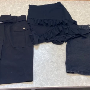 Tre svarta kjolar i olika stilar - Säljer tre svarta kjolar: en långkjol med bälte och stora fickor, en kort volangkjol med omlottkänsla och en klassisk svart jeanskjol. Perfekt för dig som vill ha olika vibes i garderoben – från casual till trendigt. Den till vänster är storlek 38, de andra två är stolek 36