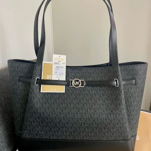 *NY* Michael Kors - Reed Large Black Monogram Tote Shoulder bag, Presenttips  - Ny oanvänd, endast packat upp plasten och lapparna. Nypris: 4400 sek, Outletpris: 2930 sek, Pris nu: 1100 sek. Kommer i MK kasse (se bilder).   En sofistikerad tote som kombinerar Michael Kors ikoniska monogram med elegant svart design och praktiska detaljer. Reed Large Tote i svart monogram med silverfärgade detaljer är ett tidlöst val för dig som vill ha en rymlig och stilfull väska för både arbete och vardag. Dator ryms utan problem. Två mindre fack, ett med blixtlås. Stängs med två knappar.