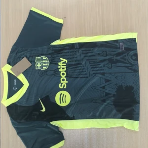 Barça Nike Dri-FIT fotbollströja S - Barcelona fotbollströja från Nike med Dri-FIT material. Tröjan är mörkgrön med neon-gula detaljer och tryck, inklusive klubbmärke och Spotify-logga på bröstet. Kortärmad modell med sportig passform och grafiskt mönster framtill. Perfekt för dig som älskar fotboll och stil.