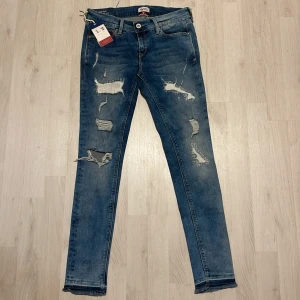 Blå slitna jeans Tommy Hilfiger - Snygga blå jeans från Tommy Hilfiger med slitna detaljer. Modellen har smal passform, och råa kanter vid benslut. Perfekta för dig som gillar en edgy streetstil. Inköpspris 950kr, oanvända med köplappen kvar.