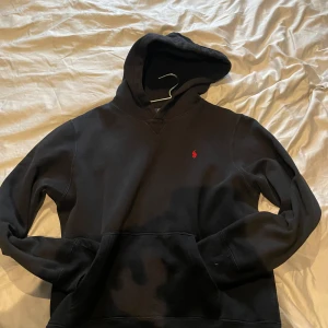 Svart hoodie från raphl lauren - Svart hoodie från Polo Ralph Lauren i storlek  18-20. Klassisk design med röd broderad logga på bröstet, stor huva och magficka. Perfekt för dig som gillar en clean och stilren look. Tillverkad i mjuk bomull för extra komfort. Snabba affärer helst, tröjan har ingen skada och köptes som ny i juni för 1000+ nånting, knappt använt så säljer den nu