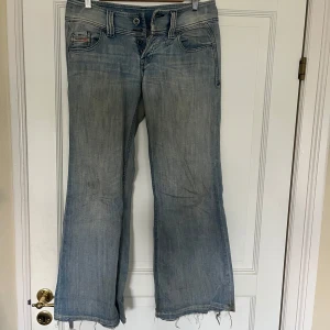 Diesel Lambry ljusblå bootcut jeans - Säljer ett par ljusblå bootcut jeans från Diesel, modell Lambry. Jeansen är lågmidjade och slitna, fransiga benslut för en avslappnad vibe. Tillverkade i  denim med snygg tvätt och diskreta detaljer på fickorna.