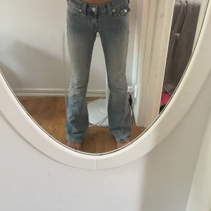 True Religion Joey Low Rise Flare Jeans - Säljer ett par ljusblå True Religion Joey jeans med låg midja och utsvängda ben. Klassiska jeansfickor med snygga detaljer och logga bak. Perfekta för dig som gillar retrovibbar och vill ha ett par jeans som sticker ut.🥰