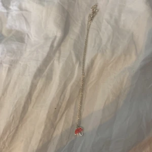Halsband med paraplyberlock i silver - Sött halsband med tunn silverfärgad kedja och en liten paraplyberlock. Berlocken är delvis röd med vita detaljer på ena sidan och helt silverfärgad på andra sidan. Perfekt accessoar för dig som gillar söta halsband.