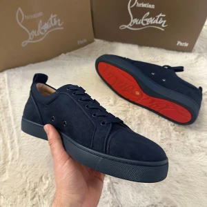 Mörkblå sneakers från Christian Louboutin - Snygga mörkblå sneakers från Christian Louboutin i mocka med klassisk röd sula och diskret broderad logga på hälen. Skorna har rund tå, snörning och en stilren design som sticker ut med den ikoniska röda undersulan. Låda, papper och allt följer med.