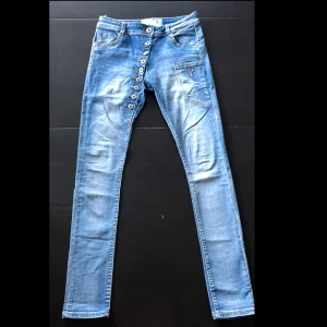 Blå skinny jeans från Chica London - Snygga ljusblå skinny jeans från Chica London med flera knappar framtill och coola detaljer på fickorna. Jeansen har klassisk femficksdesign och är tillverkade i stretchigt denim för en tight passform. Perfekta för dig som gillar en trendig och bekväm stil.