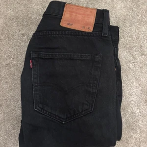 Svarta Levi's 501 jeans straight fit - Svarta Levi's 501 jeans med klassisk straight fit. Tillverkade i slitstarkt jeanstyg med knappgylf och silverfärgade nitar framtill. Jeansen är använda och lite urtvättade som ni säkert ser på bilderna, skulle säga 7/10 i cond. Storlek W31 L30 och passar mig perfekt som är 180cm och väger 70kg. 