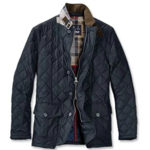 Barbour jacka - Snygg mörkblå quiltad jacka från Barbour med klassiskt rutigt innerfoder och coola detaljer som brunt spänne vid kragen. Jackan har stora fickor framtill, dragkedja och knappar. Perfekt för dig som gillar stilren och tidlös look.