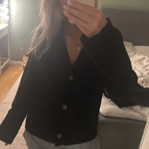 Svart stickad kofta med knappar - Svart stickad kofta med stora, snygga knappar framtill. Koftan har långärmad design och en klassisk v-ringning. Perfekt för lager-på-lager och passar till allt. Enkel och stilren look som funkar året runt.