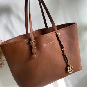 Rymlig Toteväska från Michael Kors - En så snygg rymlig väska från Michael Kors🌸Väskan har flera fack och dragkedja. Många fina detaljer. Självklart är väskan äkta (fler bilder kan skickas och på serienummer). Lite slitage på handtagen finns men inget man tänker på. Bredd:40 cm Höjd:28 cm
