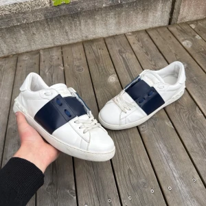 Valentino Garavani Open sneakers vit/blå - Säljer ett par Valentino Opens! Storlek 43 men är lite små i storleken. Följer även med en dustbag. Perfekta för dig som gillar stilrena och exklusiva sneakers. Hör av dig vid minsta fundering!