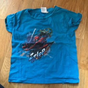 Blå Marvel Spiderman t-shirt - Cool blå t-shirt från Marvel med tryck av Spiderman och texten 'ZIPP' på framsidan. Klassisk rund hals och korta ärmar. Perfekt för dig som gillar superhjältar och vill sticka ut med en färgstark look.