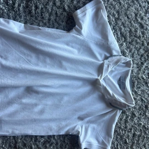 Vit pike  från Erla of Sweden - Klassisk vit t-shirt från Erla of Sweden i storlek M. T-shirten har rund halsringning och korta ärmar, tillverkad i mjuk bomull som känns skön mot huden. Perfekt basic-plagg att ha i garderoben.