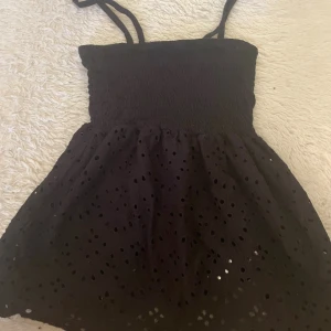 Svart fin tröja  från Primark - Supersöt svart tröja från Primark med smockad överdel och tunna axelband. Tröjan  är utsvängd och har broderade hål som ger en luftig känsla. Perfekt för varma dagar och enkel att styla med sneakers eller sandaler.