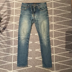 Nudie Jeans Skinny Blå 31/32 - Säljer ett par snygga skinny jeans från Nudie Jeans i klassisk ljusblå tvätt. Jeansen har orangea sömmar, fem fickor och ikonisk brodyr på bakfickorna. Perfekt passform med smala ben och normal midja. Materialet är mjukt och stretchigt jeans.