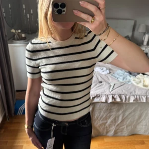 Randig ribbad topp från Gina Tricot  - Säljer en ribbad topp från Gina Tricot i krämvit med svarta horisontella ränder. Modellen är croppad med korta ärmar och rund halsringning. Den är i mycket fint skick då jag inte har använt den mer än två gånger. Hör gärna av dig vid frågor🤎