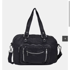 Svart axelväska från Núnoo i skinn - Svart trendig axelväska från Núnoo i äkta skinn med flera dragkedjefickor framtill och justerbar axelrem. Rymmer väldigt mycket! Köptes på Åhléns för 2658kr, men säljes då den inte kommer till användning längre! Väskan är i mycket fint skick!