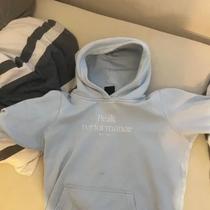Ljusblå hoodie från Peak Performance - Snygg ljusblå hoodie från Peak Performance med broderad logga framtill. Klassisk känguruficka och huva, perfekt för chill dagar. Mjuk bomullsblandning som känns skön mot huden. Enkel och stilren design som funkar till det mesta.